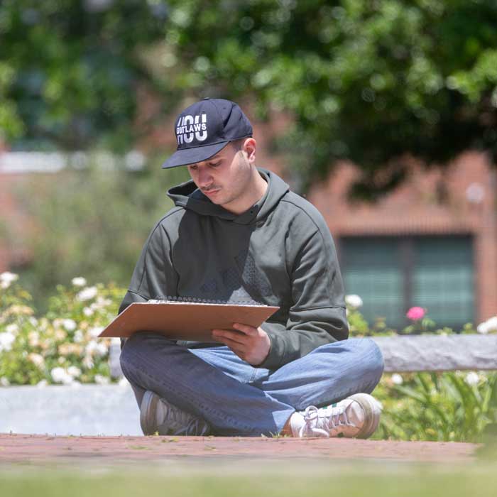 student sitting outside and sketching in a large sketch book