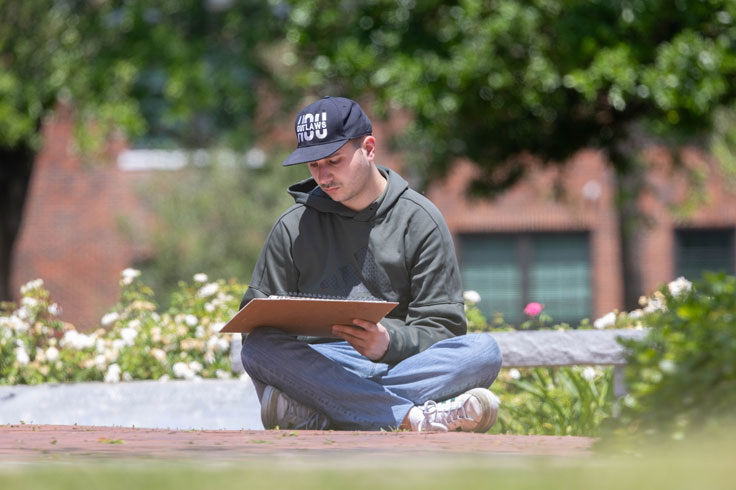 student sitting outside and sketching in a large sketch book